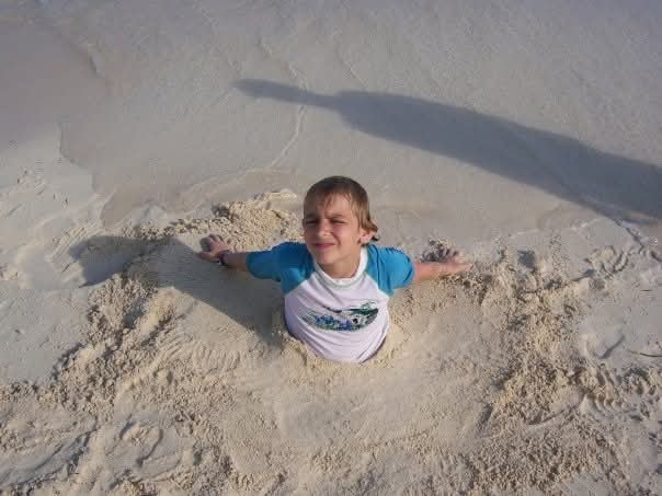 Young boy buried in the sand at the beach, smiling