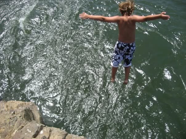 Boy jumping off rocks into the water arms outstretched