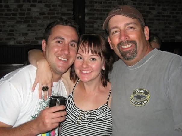 Three friends smiling together at a bar with Kona Brewing shirts