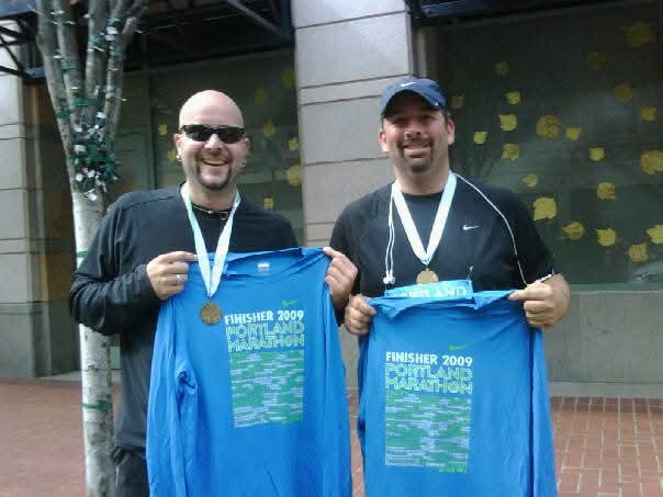 Two friends holding Portland Marathon finisher shirts and medals