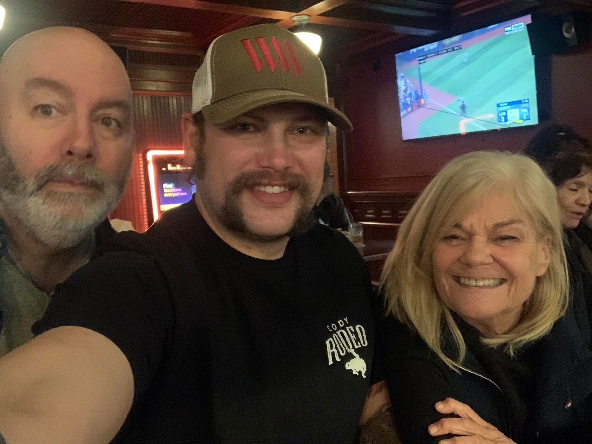 Three friends smiling at a bar watching sports